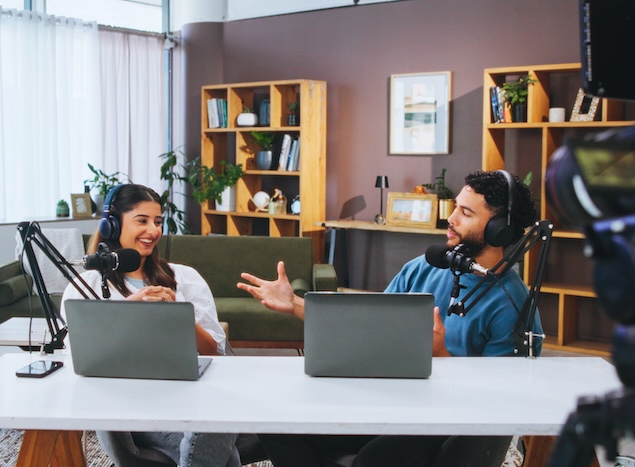 A man and a woman wearing headphones filming a podcast in a home studio